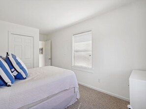 A bedroom with a bed, a white door, a window with blinds, and a white cabinet.
