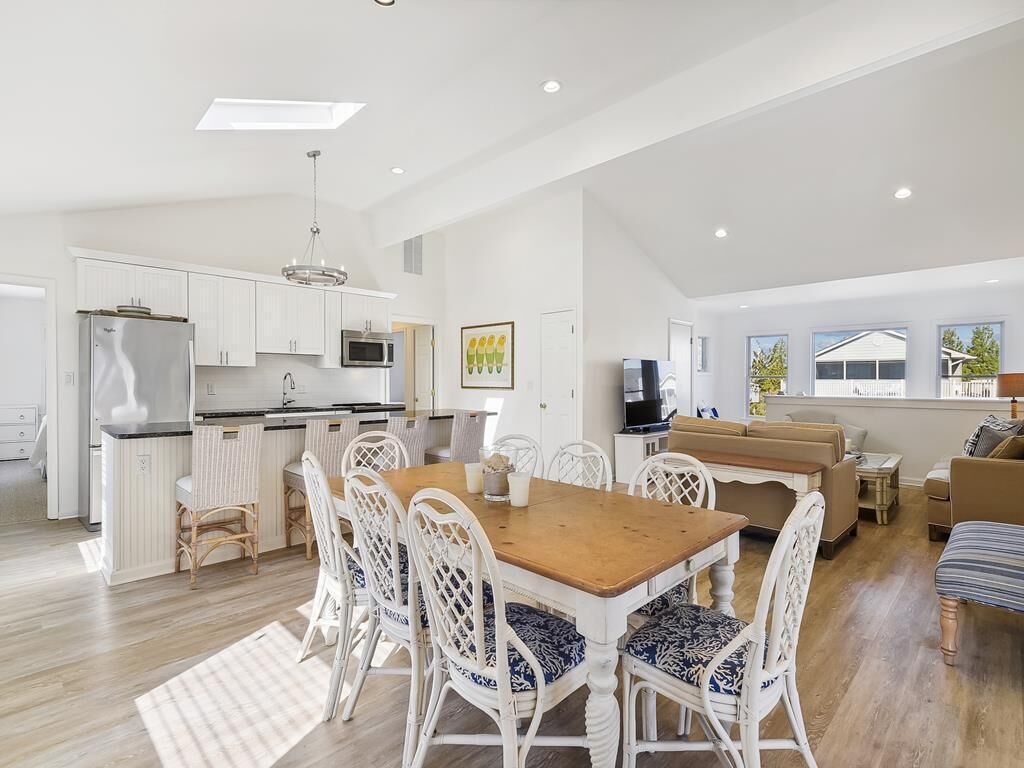 Une cuisine spacieuse avec des meubles blancs, un îlot central et un coin repas comprenant une table en bois et des chaises blanches.