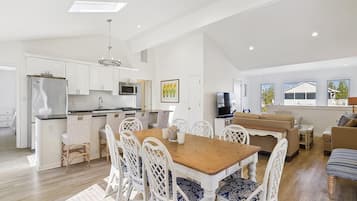 Une cuisine spacieuse avec des meubles blancs, un îlot central et un coin repas comprenant une table en bois et des chaises blanches.