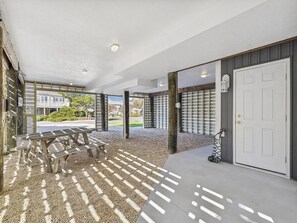 An outdoor covered area with a picnic table, a door, and a view of a building in the background.