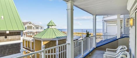 A covered balcony with a view of the beach, white outdoor furniture, and a gazebo.