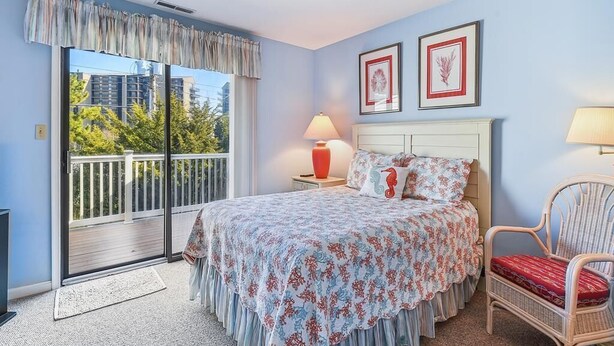 A bedroom with a bed, a chair, a nightstand, a lamp, a window with a view, and two framed pictures on the wall.