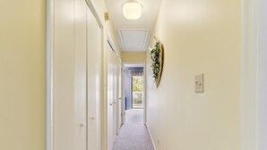 A hallway with a carpeted floor, a ceiling light, and a door on the left.