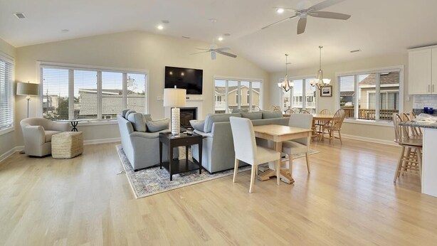 A spacious living room with a sofa, dining table, and chairs, a fireplace, and a ceiling fan. - 6-Bedroom Beach House w/ Ocean Views (South Bethany Beach)