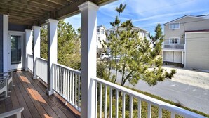 A covered porch with white railings, a wooden ceiling, and a view of residential buildings and a street. - 6-Bedroom Beach House w/ Ocean Views (South Bethany Beach)