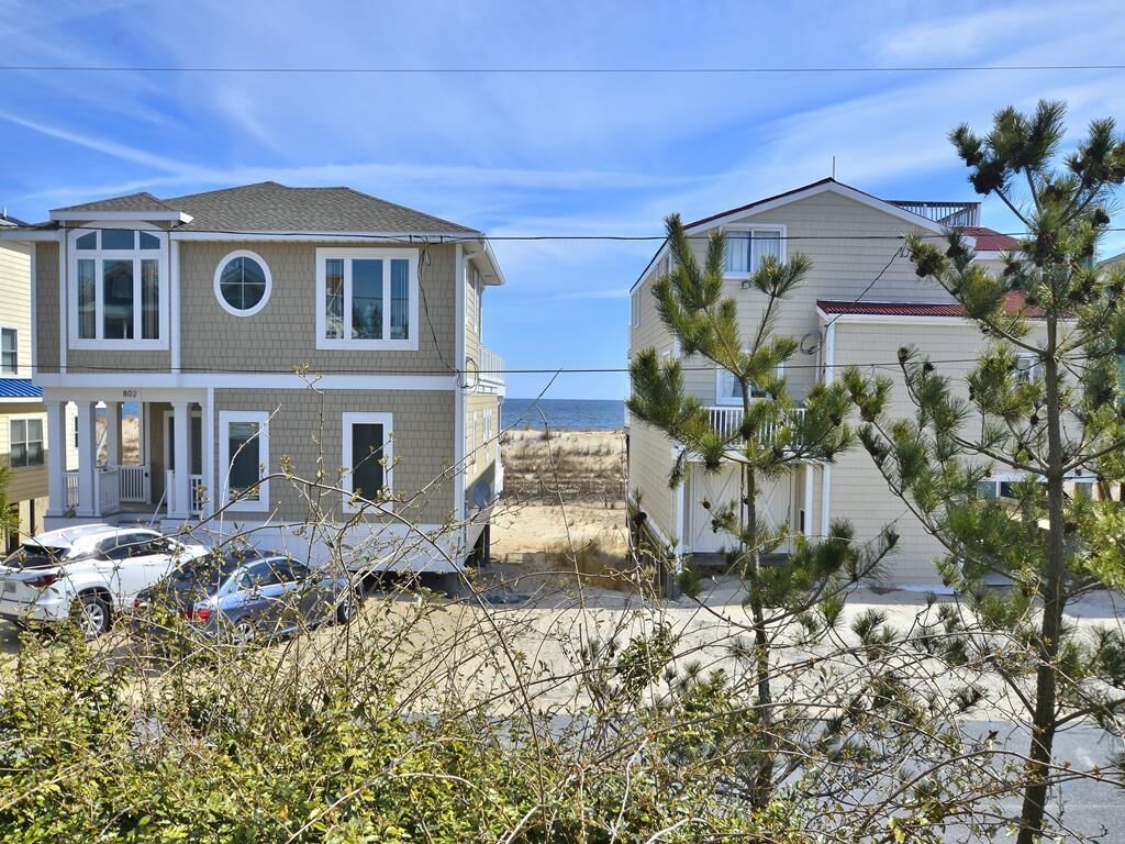 A two-story residential building with a front porch, a garage, and a driveway with parked cars.