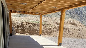 Un espace extérieur abrité, doté d’un sol en béton et de poutres en bois, qui offre une vue sur une colline rocheuse.