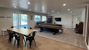 Une pièce spacieuse avec une grande table à manger en bois, plusieurs chaises, un billard et un téléviseur fixé au mur.