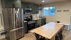 Une cuisine moderne dotée d’appareils électroménagers en acier inoxydable, d’une table à manger en bois et de meubles de rangement verts.