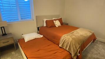 A bedroom with two beds, a ceiling fan, a nightstand, and a window with blinds.