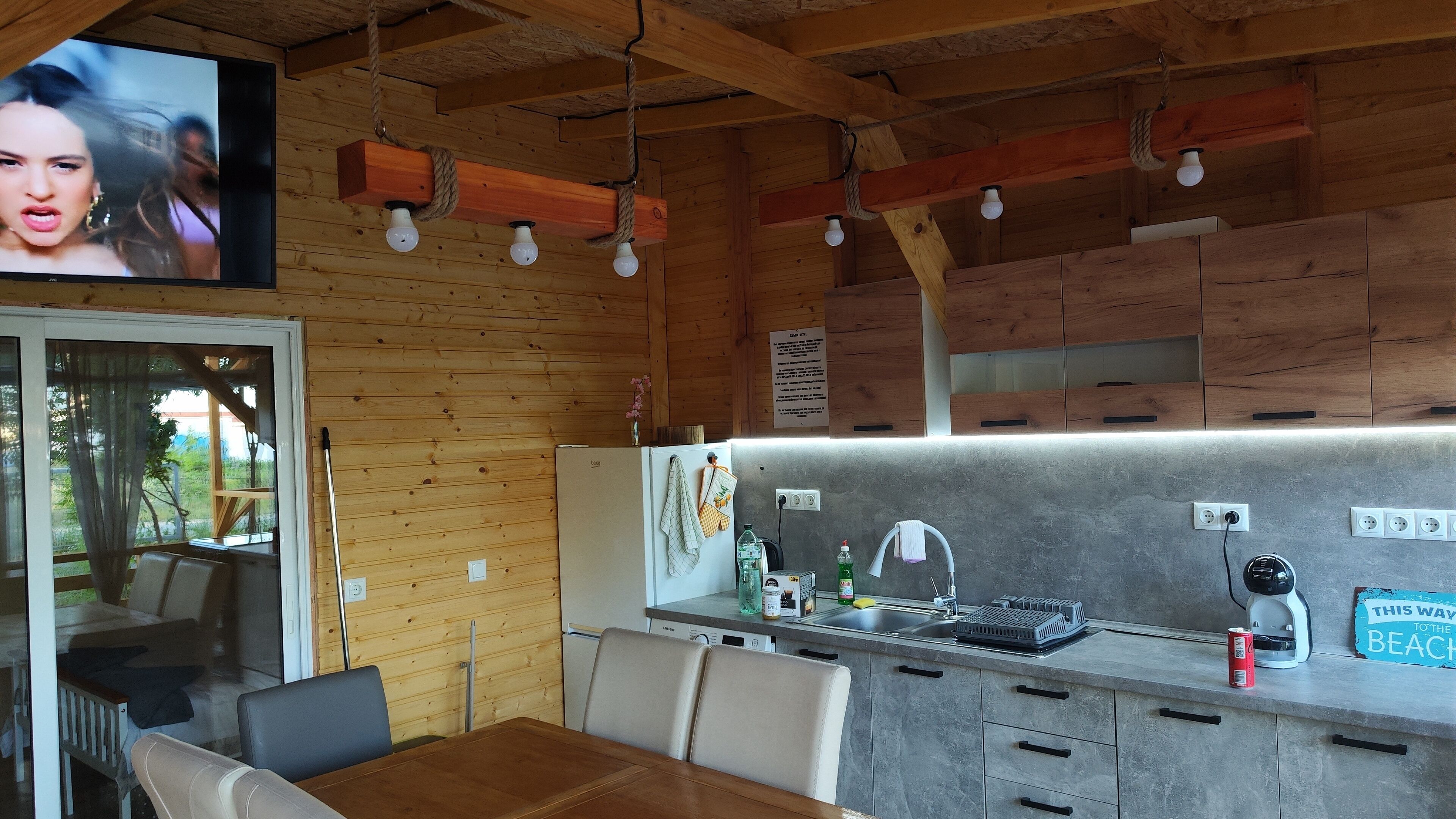 A cozy cabin-style kitchen with wooden walls, a dining area with a table and chairs, and a TV mounted above the kitchen.