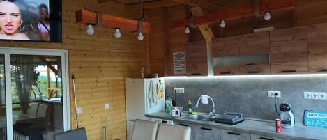 A cozy cabin-style kitchen with wooden walls, a dining area with a table and chairs, and a TV mounted above the kitchen.