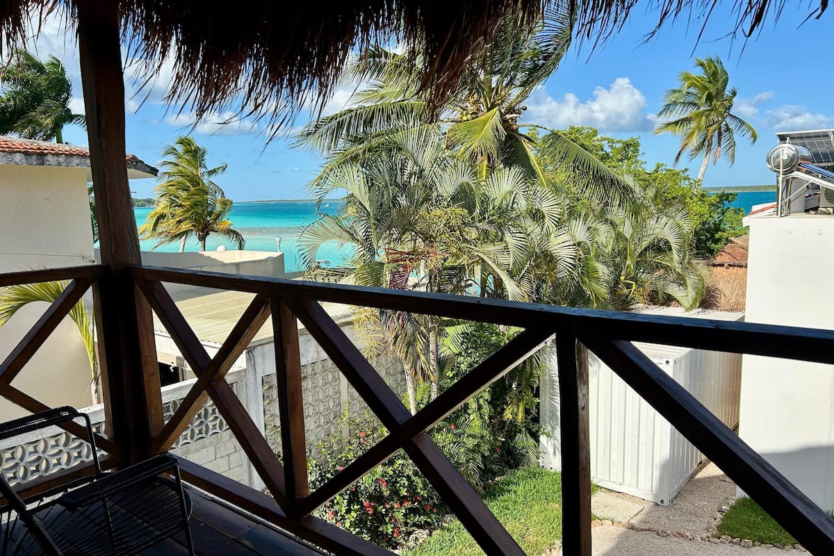Un balcon avec vue sur une plage, des palmiers et un ciel bleu azur.