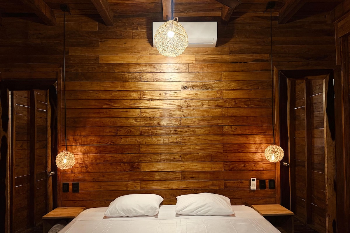 Una habitación con paneles de madera, una cama, dos lámparas de noche y un candelabro en el techo.
