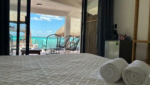 Ein Hotelzimmer mit Bett, Meerblick, einem Balkon mit Sitzgelegenheiten und einer Minibar.