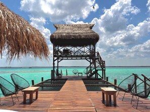 A wooden deck leading to a thatched-roof structure with a view of turquoise waters. - Hotel Solana Bacalar (Bacalar)