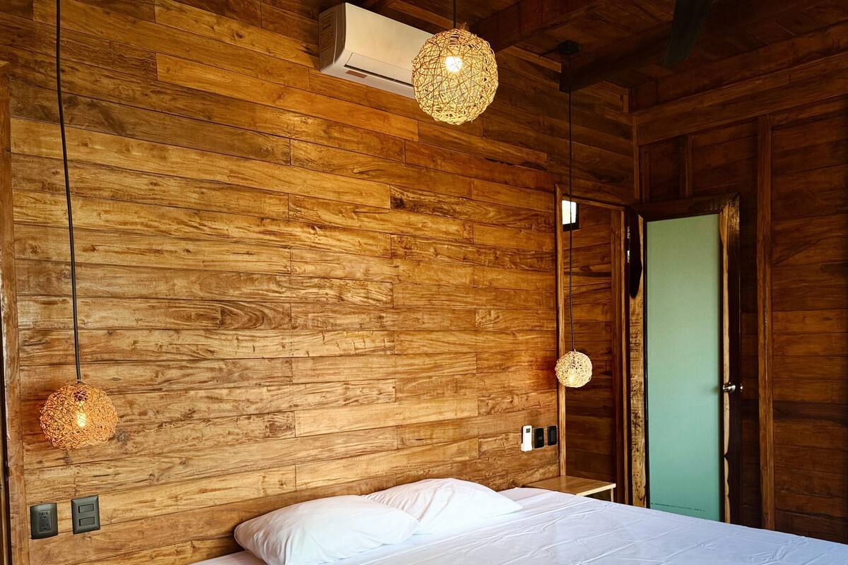 Une pièce aux murs lambrés, avec un lit, deux lampes fixées au mur et une porte verte.