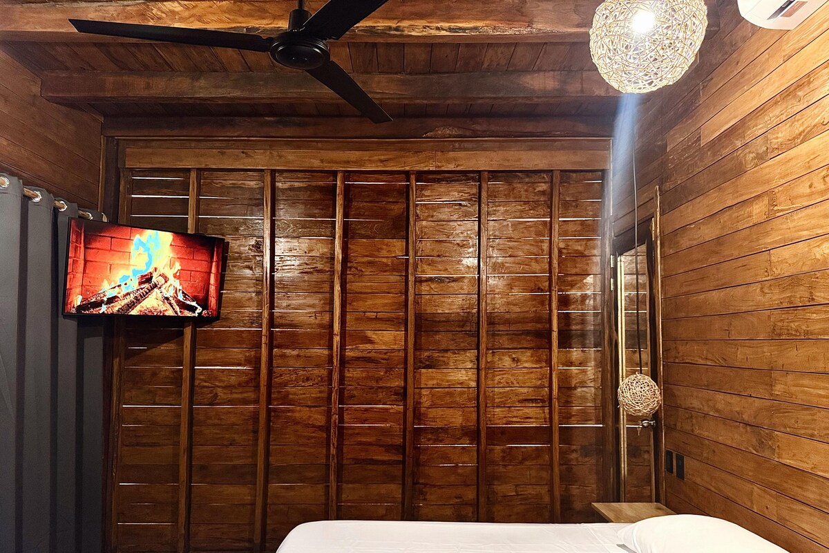 A wooden-paneled room with a bed, a ceiling fan, a mounted TV, and a decorative spherical object on the wall.