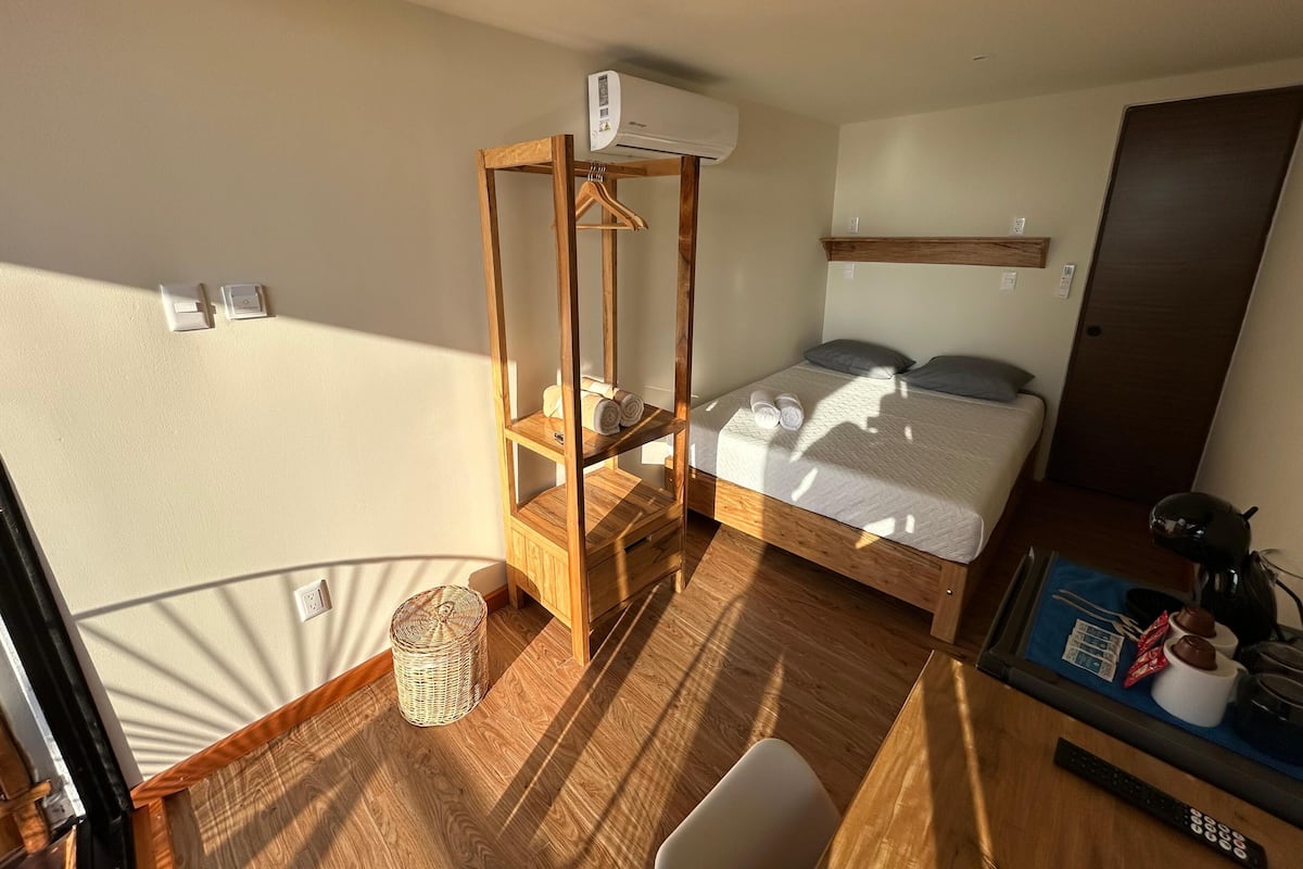 Une pièce comprenant un lit, une étagère en bois, un panier en osier et un bureau avec une télécommande.