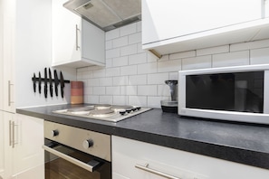 A modern kitchen with white cabinets, a gas stove, a microwave, and a knife rack.