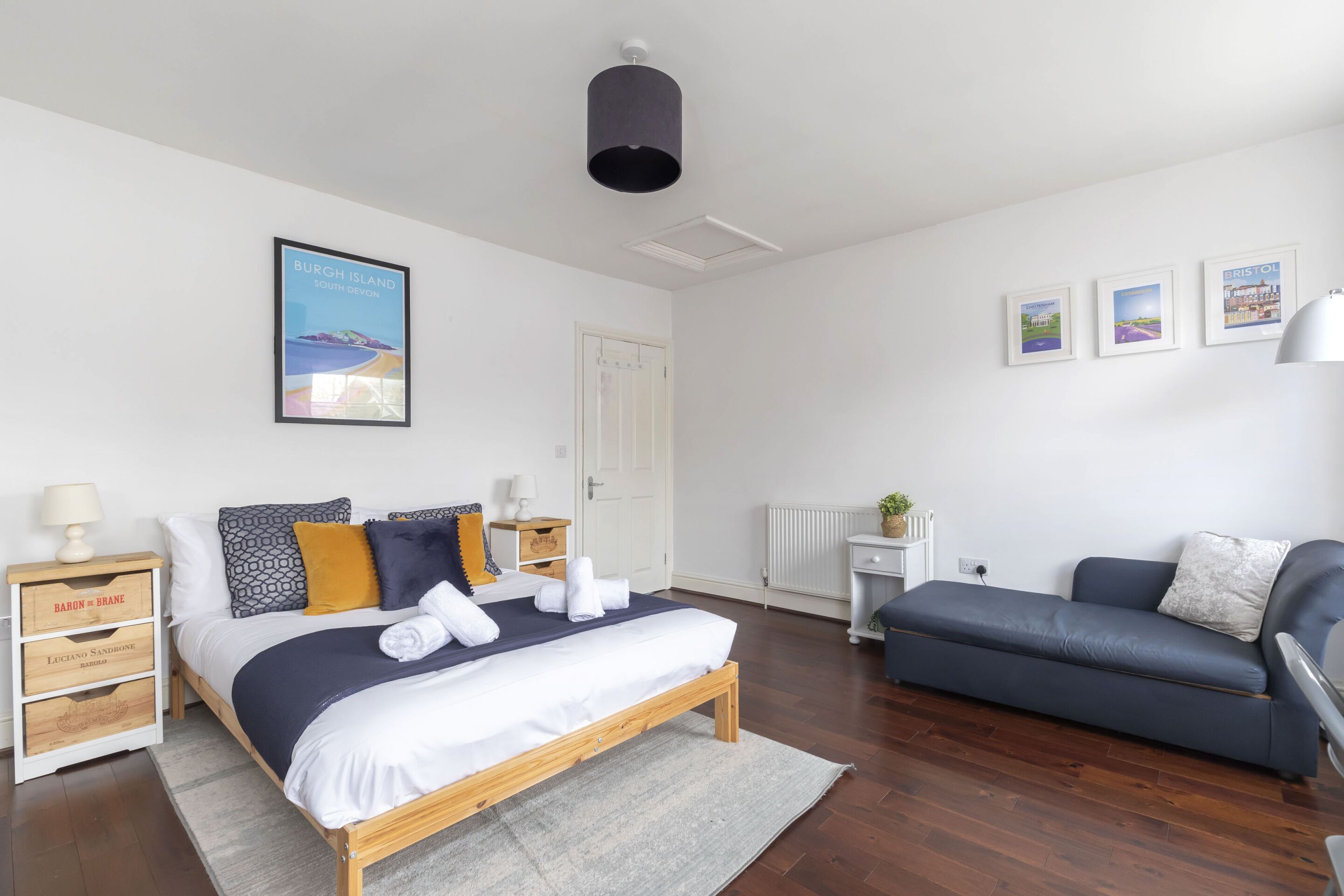 Een slaapkamer met een bed, een blauwe bank, een witte radiator en ingelijste foto’s aan de muur.