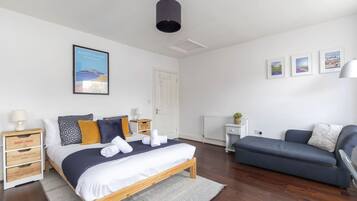 Een slaapkamer met een bed, een blauwe bank, een witte radiator en ingelijste foto’s aan de muur.