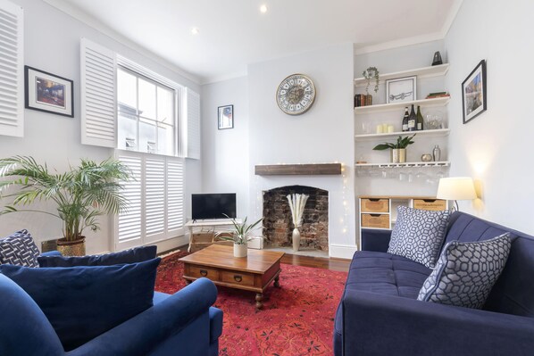 A living room with a fireplace, a TV, and a coffee table. - Lovely 2-Bed Town Centre Duplex Apartment (Gloucestershire)