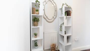Een witte ruimte met twee witte wandplanken, elk met boeken en potplanten. Een grote spiegel hangt aan de muur ertussen.