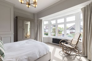 Ein Schlafzimmer mit einem großen Bett, einem Schaukelstuhl, einem Fenster mit Vorhängen und einer Heizung.