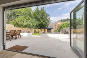 Un patio con una mesa y sillas, una cerca de madera y un jardín con diversas plantas.