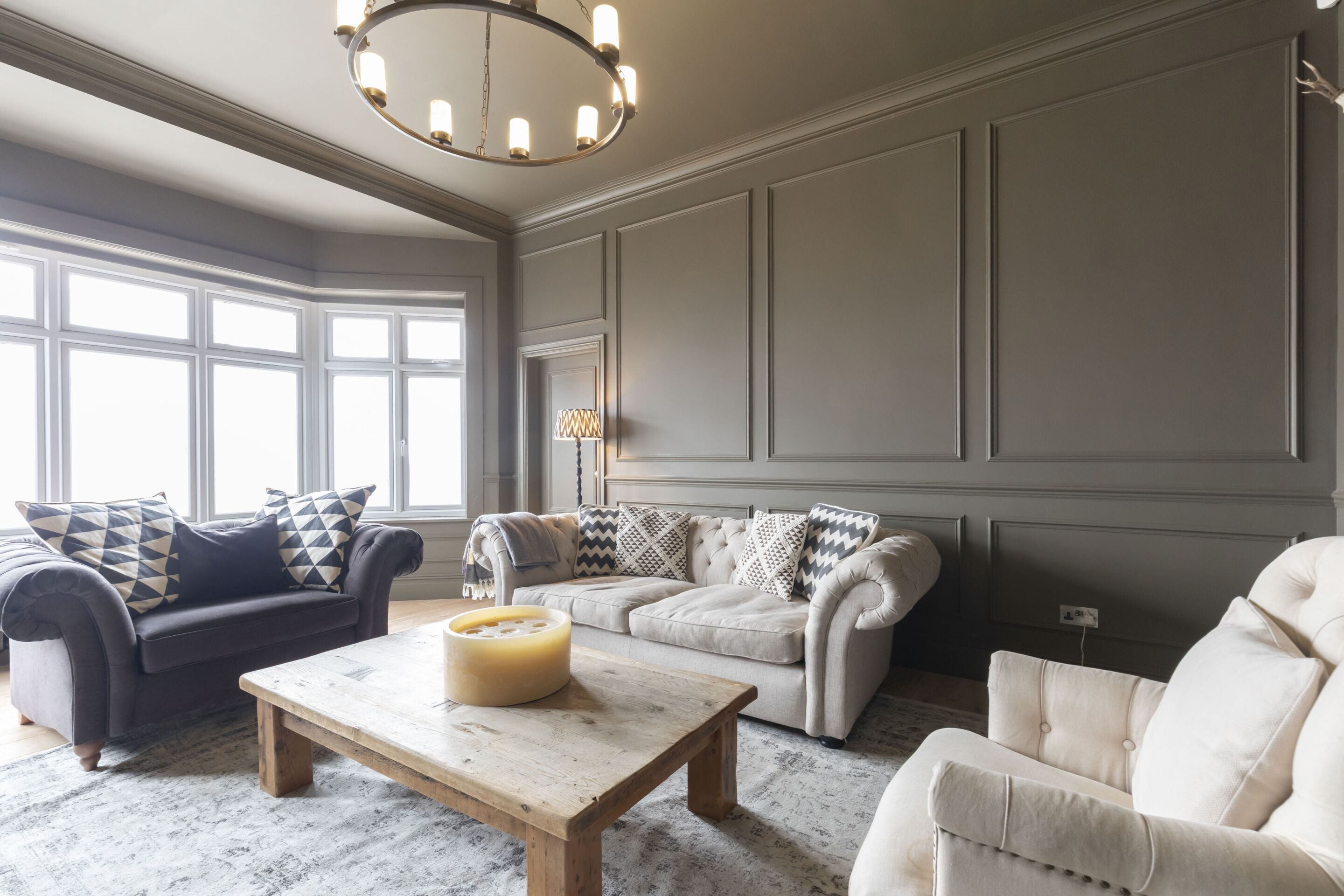 Un salon spacieux avec un mur gris, une table basse en bois et deux canapés ornés de coussins à motifs.