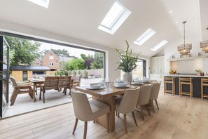 A spacious dining area with a large table and chairs, a kitchen with a marble countertop, and a view of the outside. - Luxury 6 Bedroom Period Home with Sauna and Gym (Gloucestershire)