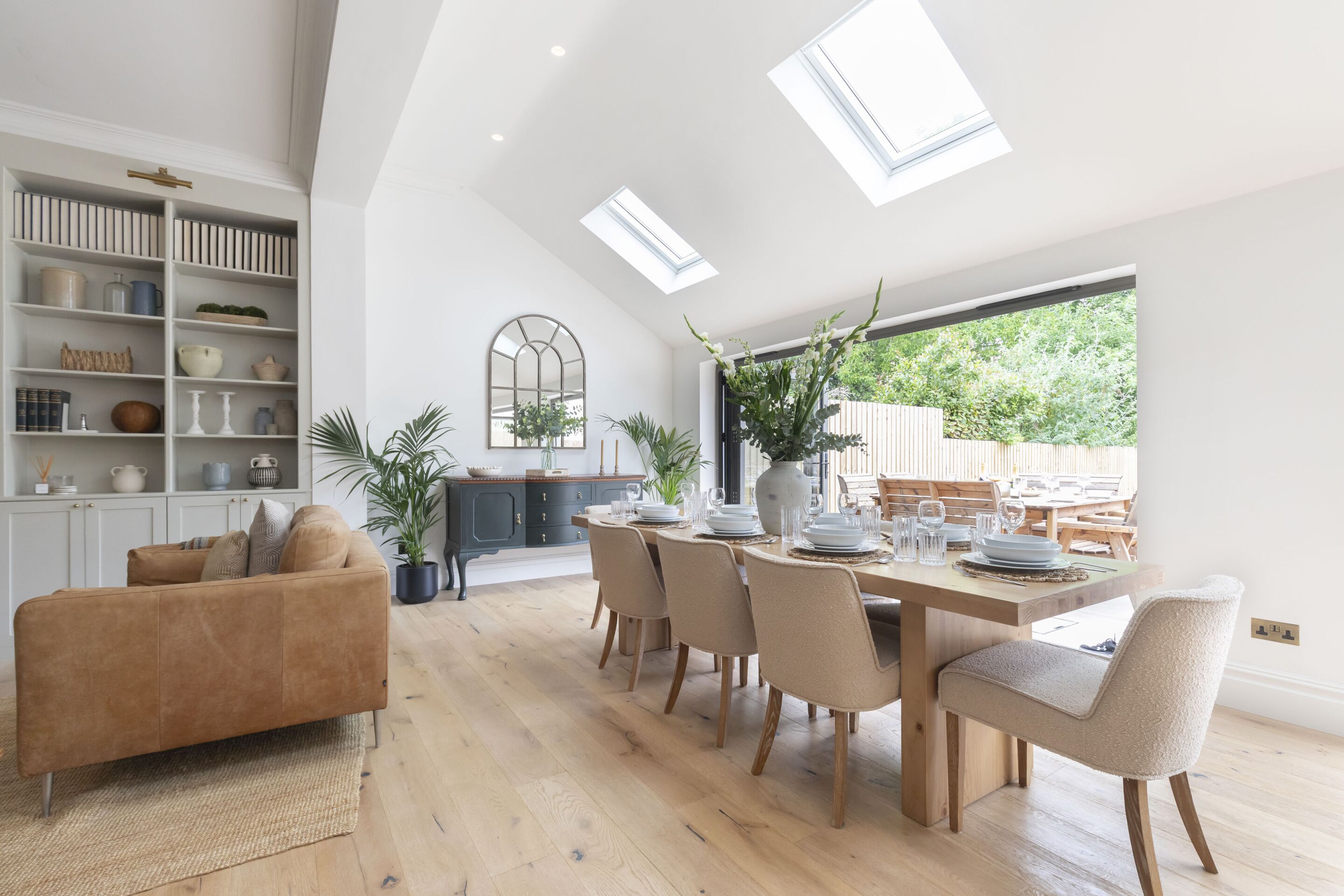 A modern dining area with a high ceiling, skylights, and a view of greenery outside.