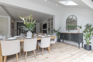 Un comedor con una mesa de madera dispuesta para cuatro personas, rodeada de sillas. Hay un jarrón grande con flores sobre la mesa, y un mueble oscuro con cajones a la derecha.