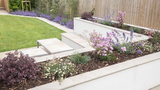 A landscaped garden with a wooden fence, a grassy lawn, and a variety of flowering plants.