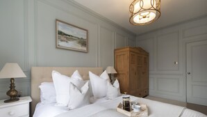 Une chambre à coucher avec un grand lit, du linge de lit blanc, une armoire en bois et un tableau accroché au mur.