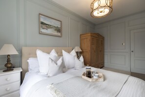 A bedroom with a large bed, white bedding, a wooden wardrobe, and a painting on the wall.