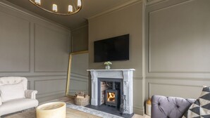 A living room with a fireplace, a sofa, a coffee table, and a television mounted on the wall. - Luxury 6 Bedroom Period Home with Sauna and Gym (Gloucestershire)