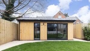 A wooden structure with a glass door, likely a shed or storage unit, in a backyard with a lawn. - Luxury 6 Bedroom Period Home with Sauna and Gym (Gloucestershire)