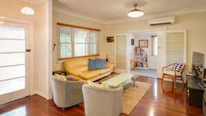 A living room with a yellow sofa, two armchairs, a glass coffee table, and a bookshelf. - Pebbles by the Bay - Quaint Central Busselton (Busselton)