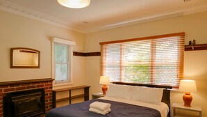 A hotel room with a large bed, two bedside lamps, a fireplace, and a window with blinds. - Pebbles by the Bay - Quaint Central Busselton (Busselton)