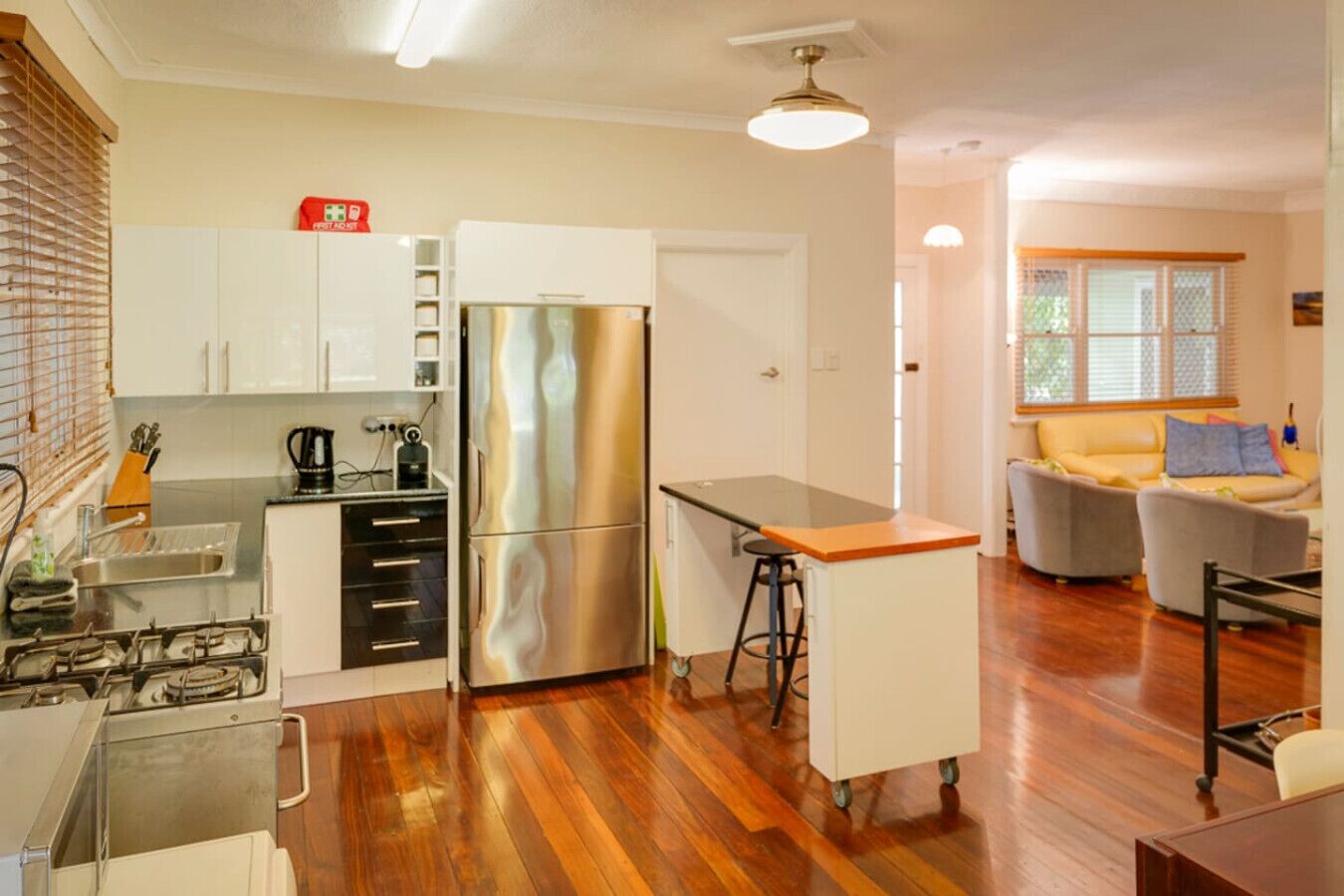 Cozinha compacta com geladeira, fogão e banquetas. Uma pequena mesa de jantar e um sofá estão na área de estar adjacente.