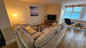 A living room with a sectional sofa, a flat-screen TV, a lamp, and a window with a view.