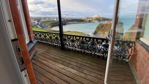 A balcony with a view of the coastline, a brick wall, and a metal railing.