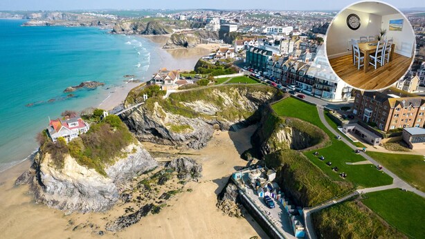 An aerial view of a coastal area with a beach, rocky cliffs, and a residential building complex.