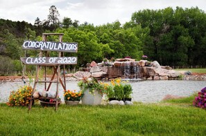 Un cartel de felicitación para la promoción de 2020, un estanque con cascada y vegetación circundante.
