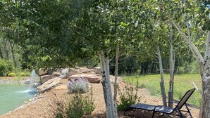 Un espace extérieur paisible, aménagé avec deux fauteuils confortables et un petit étang, le tout entouré d’arbres et de rochers.
