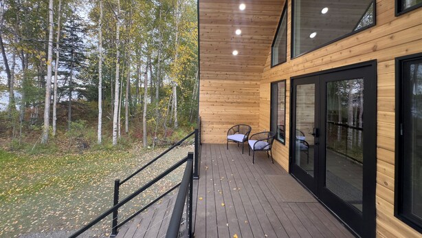 A wooden deck with a railing, large windows, and a view of a forest. - Lakefront Cottage with Sauna- #3 Chinook (Wasilla)