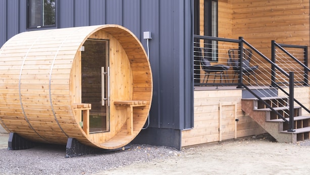Uma sauna de madeira anexa a um edifício moderno, com varanda e escadas.