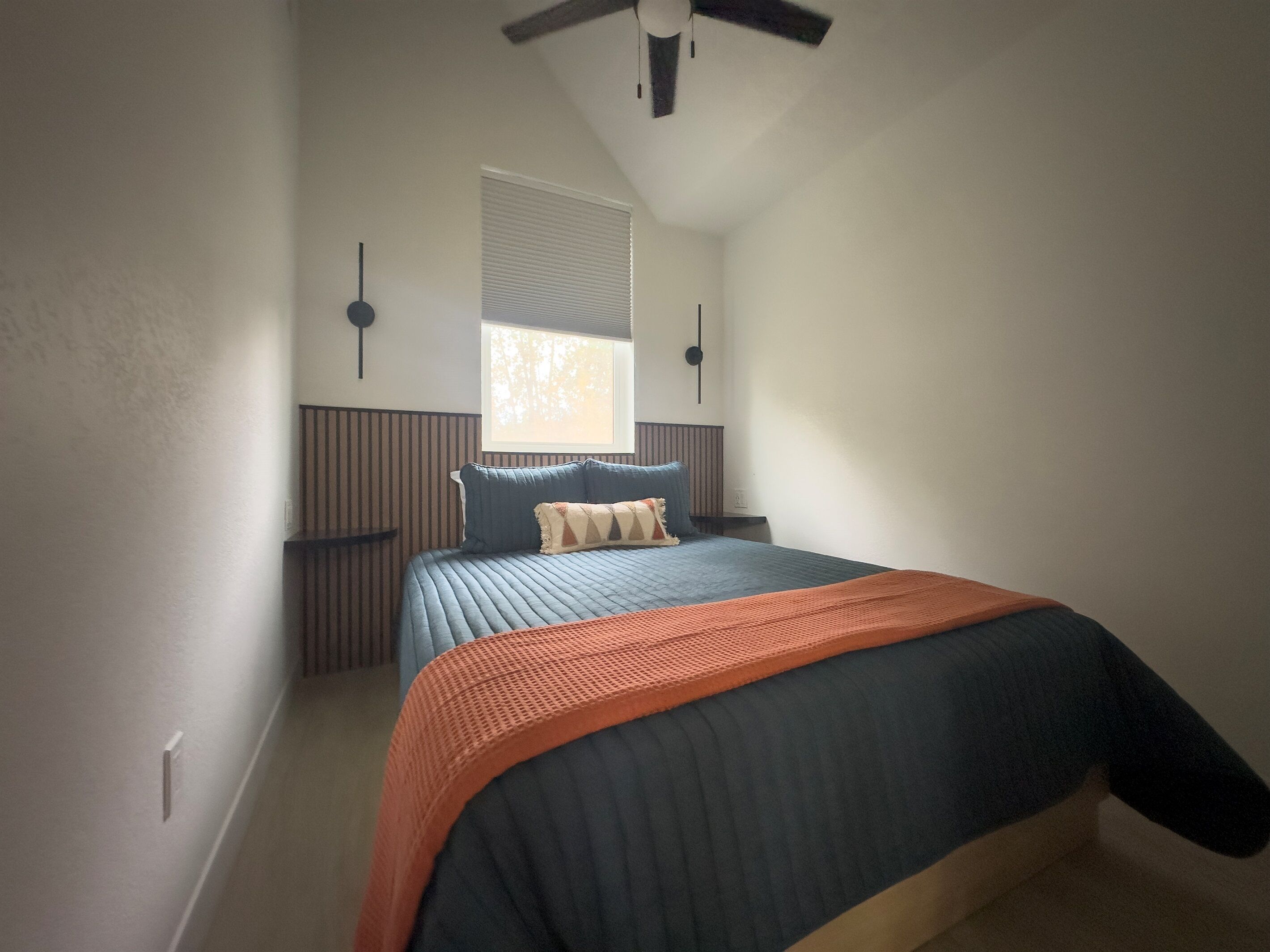 Une chambre à coucher avec un lit, une fenêtre, un ventilateur de plafond et une table de chevet.